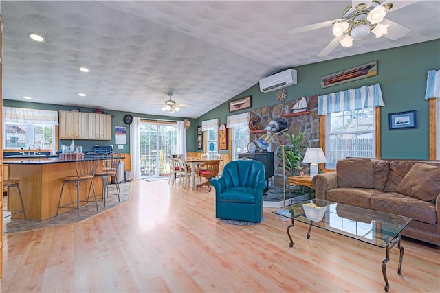 living area featuring a ceiling fan, a wall mounted AC, plenty of natural light, and light wood-style floors