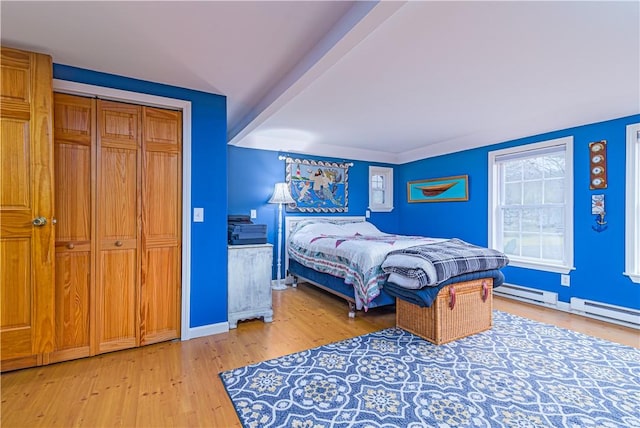 bedroom with baseboards, light wood-type flooring, a baseboard radiator, and a closet