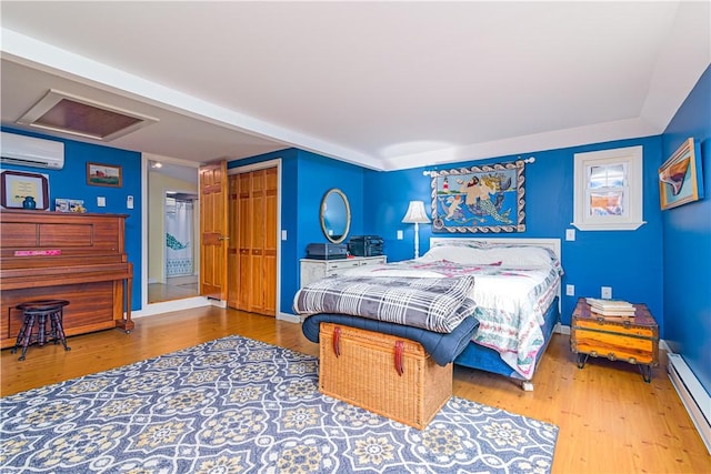 bedroom with wood finished floors, an AC wall unit, attic access, and a baseboard radiator