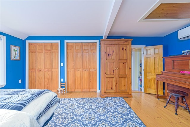 bedroom with vaulted ceiling with beams, multiple closets, a wall mounted AC, and wood finished floors