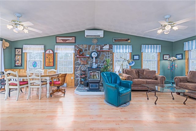 living room featuring a wall unit AC, wood finished floors, a wood stove, and a ceiling fan