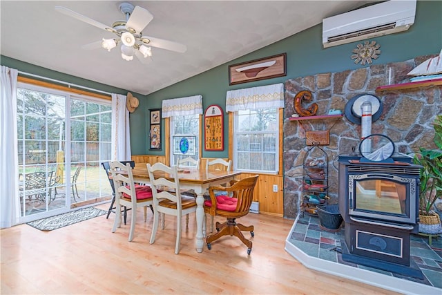 dining space featuring lofted ceiling, a wood stove, a wainscoted wall, a wall mounted air conditioner, and wood finished floors
