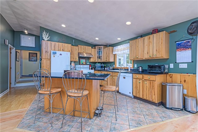 kitchen with a kitchen island, a breakfast bar, under cabinet range hood, white appliances, and dark countertops