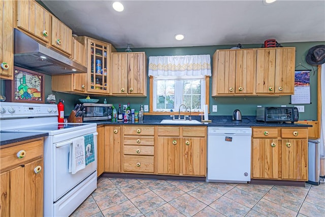 kitchen with white appliances, dark countertops, under cabinet range hood, and a sink