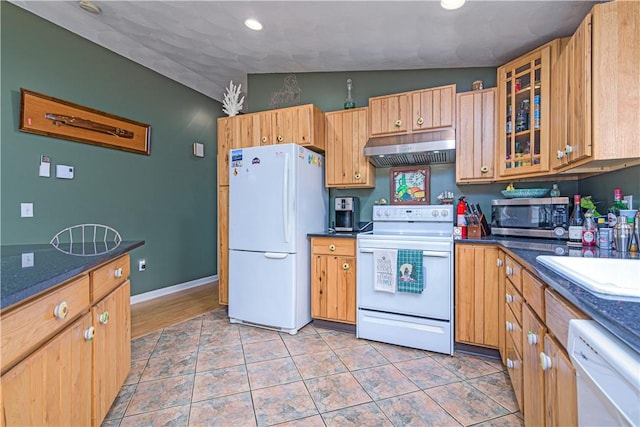 kitchen featuring white appliances, under cabinet range hood, glass insert cabinets, a sink, and light tile patterned floors