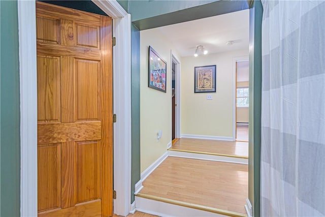 hall with baseboards, wood finished floors, and a baseboard heating unit