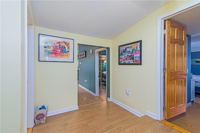 hallway with baseboards, light wood-style floors, and lofted ceiling