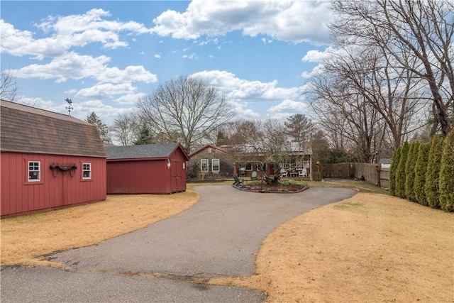 exterior space featuring aphalt driveway, an outbuilding, a storage unit, and fence