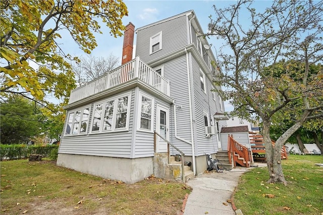 exterior space with a front lawn, entry steps, a chimney, and a balcony