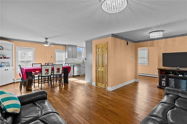 living area with ceiling fan with notable chandelier, hardwood / wood-style flooring, and crown molding