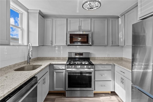 kitchen with a sink, light stone countertops, tasteful backsplash, appliances with stainless steel finishes, and gray cabinetry
