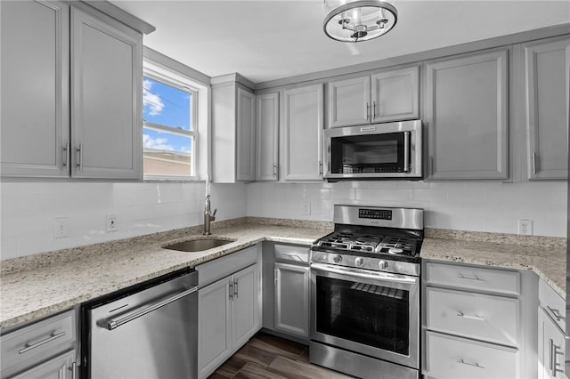 kitchen with backsplash, a sink, gray cabinetry, stainless steel appliances, and dark wood-type flooring