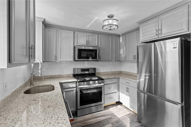 kitchen featuring light stone countertops, stainless steel appliances, tasteful backsplash, a sink, and gray cabinets
