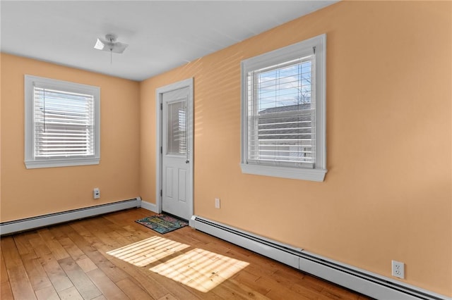 foyer entrance with wood finished floors, a baseboard heating unit, and a wealth of natural light