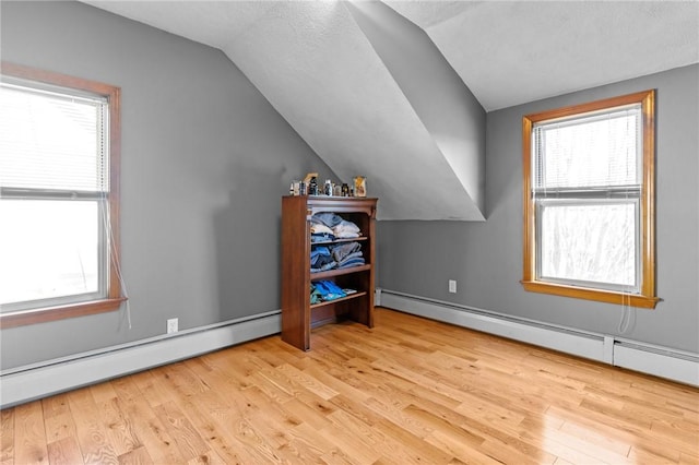 additional living space featuring a baseboard radiator, a wealth of natural light, a baseboard heating unit, and wood finished floors