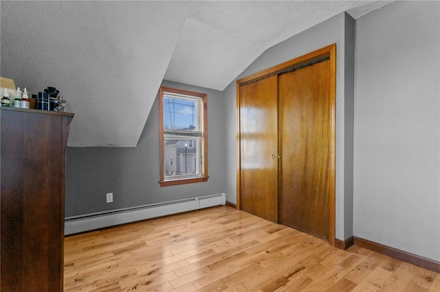 unfurnished bedroom featuring a closet, light wood finished floors, baseboards, a baseboard radiator, and vaulted ceiling