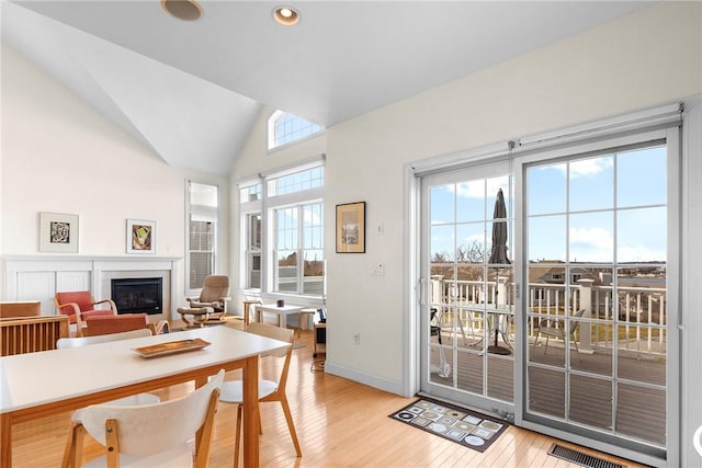 dining room featuring vaulted ceiling, light wood finished floors, a glass covered fireplace, baseboards, and visible vents