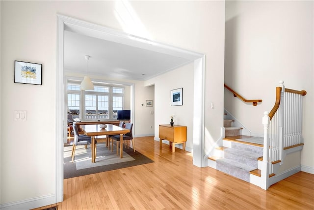 dining area with baseboards, stairway, ornamental molding, and light wood-style floors