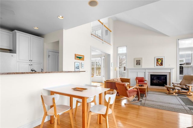 dining room featuring high vaulted ceiling, recessed lighting, a glass covered fireplace, and light wood-type flooring