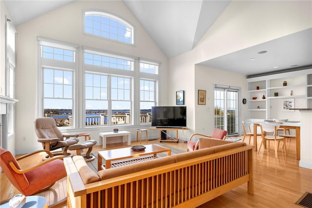 living room featuring light wood finished floors, baseboards, visible vents, and high vaulted ceiling