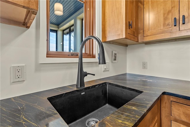 kitchen view of a sink, brown cabinets, and dark stone countertops