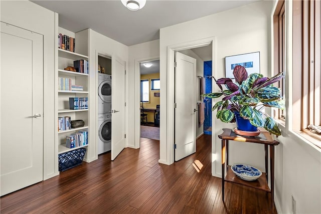 laundry area with estacked washer and dryer, dark wood-type flooring, and baseboards
