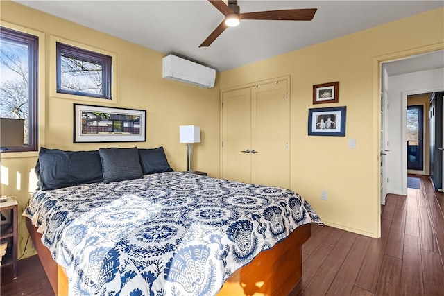 bedroom with a wall mounted AC, a closet, dark wood finished floors, ceiling fan, and baseboards