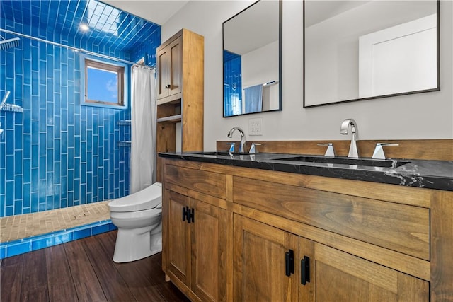 full bathroom featuring toilet, tiled shower, double vanity, and wood finished floors