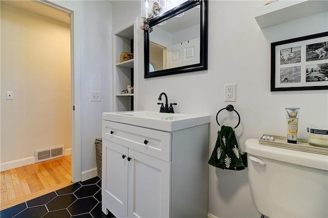 bathroom with vanity, baseboards, toilet, visible vents, and wood finished floors