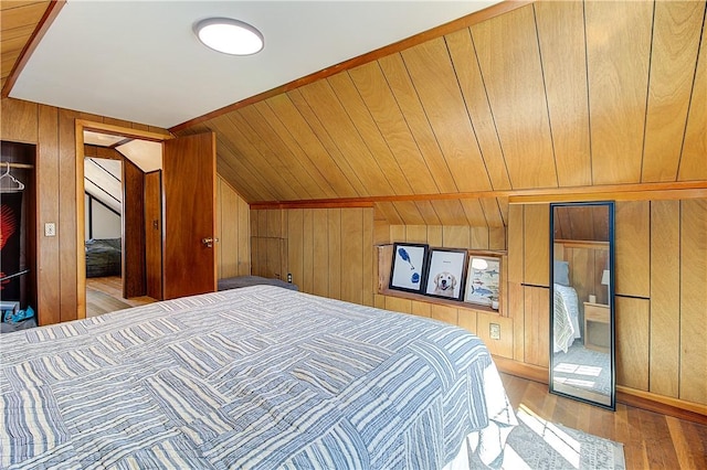 bedroom featuring light wood finished floors, wood walls, and lofted ceiling