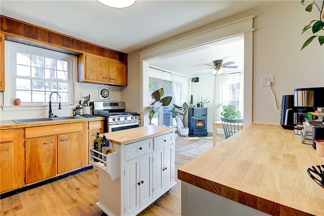 kitchen with a wealth of natural light, a wood stove, a sink, and stainless steel range with gas cooktop