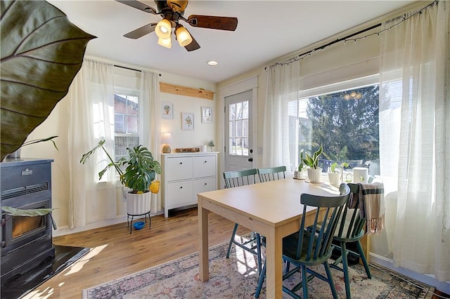 dining space featuring a wood stove, a ceiling fan, plenty of natural light, and wood finished floors