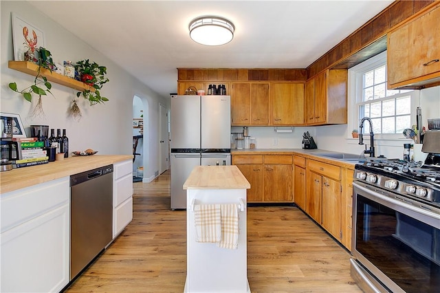 kitchen featuring arched walkways, light wood-style flooring, a sink, and appliances with stainless steel finishes