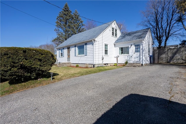 view of front facade with aphalt driveway, roof with shingles, entry steps, and fence