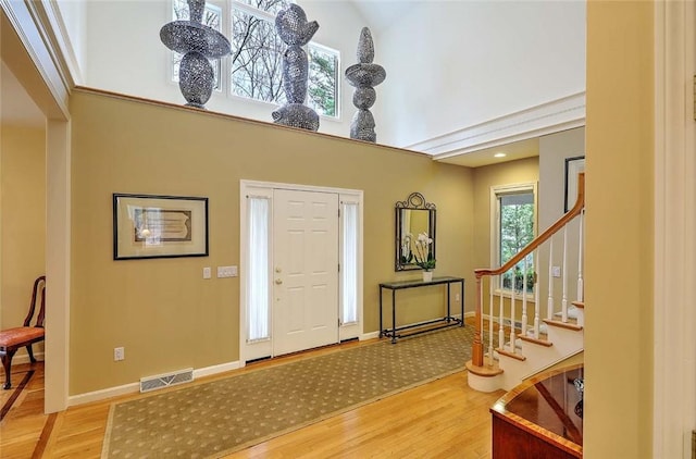 entryway with visible vents, stairs, wood finished floors, baseboards, and a high ceiling