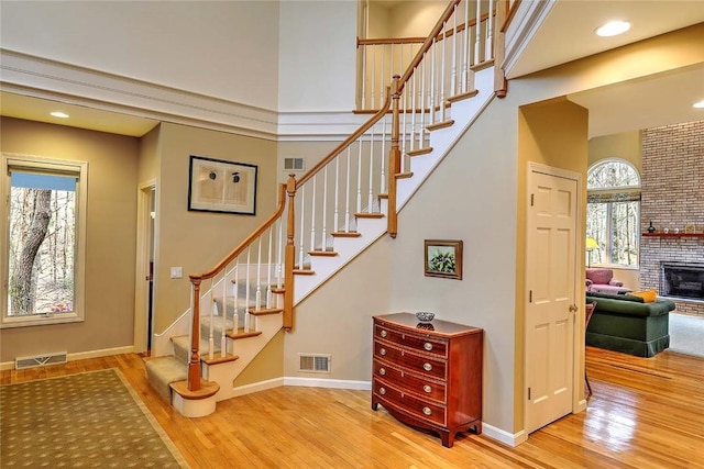 staircase featuring a brick fireplace, wood finished floors, and visible vents