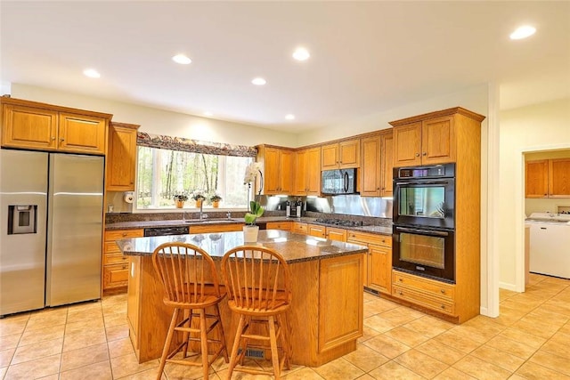 kitchen with washer / clothes dryer, a center island, brown cabinets, black appliances, and recessed lighting