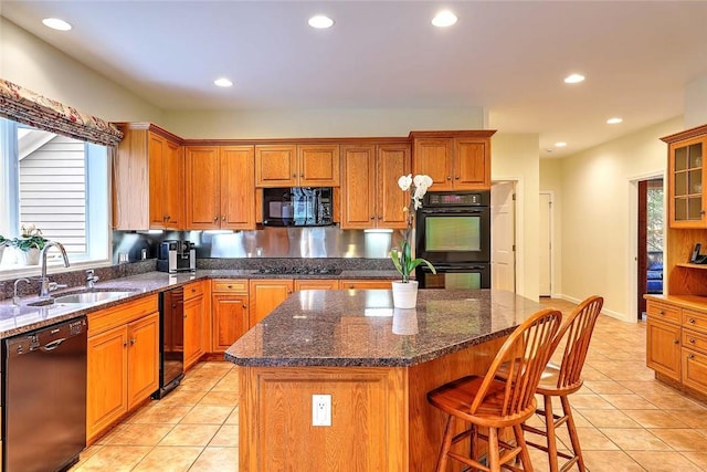 kitchen with a breakfast bar area, brown cabinets, a sink, light tile patterned floors, and black appliances
