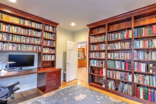 office space with recessed lighting, wall of books, and light wood-style floors