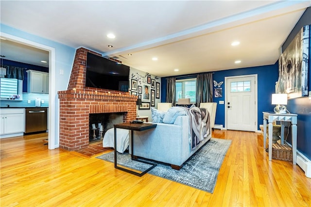 living room with a brick fireplace, beamed ceiling, recessed lighting, light wood finished floors, and a baseboard heating unit