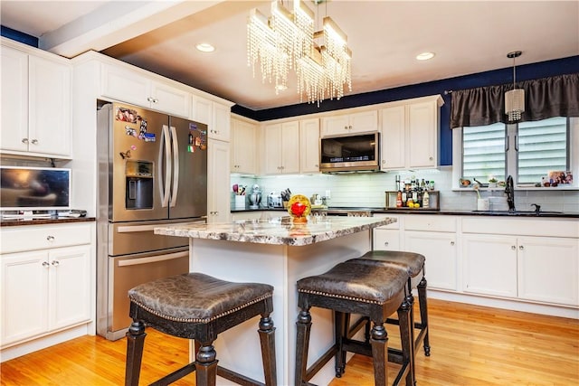 kitchen with light wood-style flooring, white cabinetry, a kitchen bar, appliances with stainless steel finishes, and a sink