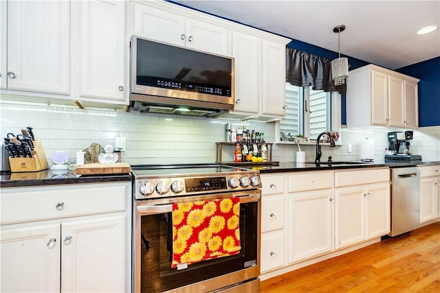 kitchen featuring tasteful backsplash, a sink, appliances with stainless steel finishes, dark countertops, and light wood finished floors