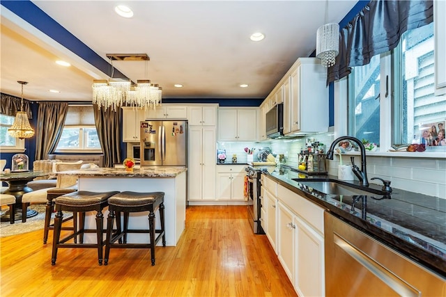 kitchen with light wood-style floors, pendant lighting, a chandelier, appliances with stainless steel finishes, and a sink