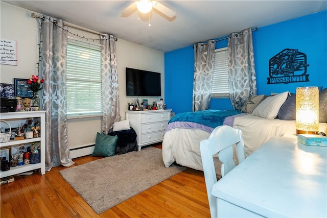 bedroom with a ceiling fan, wood finished floors, and baseboard heating