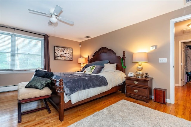 bedroom with baseboard heating, baseboards, visible vents, ceiling fan, and wood finished floors
