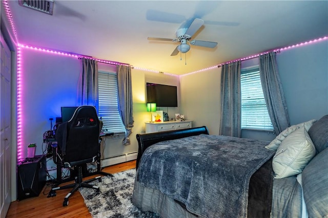 bedroom with wood finished floors, a baseboard heating unit, a ceiling fan, and visible vents