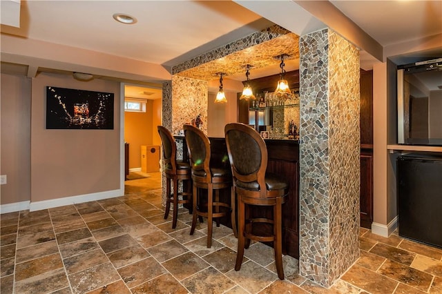 bar with decorative light fixtures, bar area, baseboards, and stone tile flooring