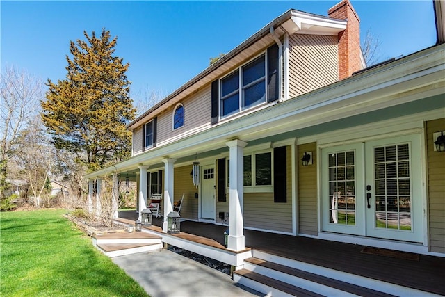 view of front facade with a porch, french doors, a chimney, and a front lawn