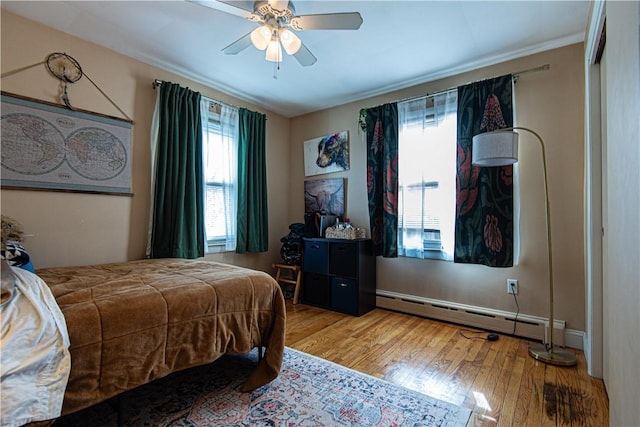 bedroom with wood finished floors, a baseboard heating unit, and a ceiling fan