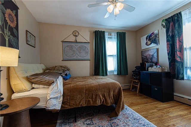 bedroom featuring light wood finished floors, baseboard heating, baseboards, and ceiling fan